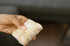 A close-up photo of a hand holding a folded stack of R20 bank notes against a blurry background