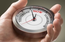 A close-up photo of a hand holding a watch with the words ‘yesterday’, ‘now’ and ‘tomorrow’ on a light background