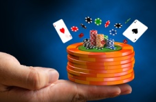 A close-up image of a hand with a stack of casino chips balancing on the fingertips and two Aces on a blue background