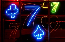 A colourful neon light sign with 7s and card symbols on a dark background