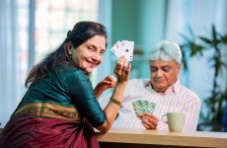 A photo of an Indian woman displaying three of a kind in aces with her husband in the back ground