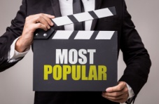 A photo of a man in a suit holding a clapper reading ‘most popular’ on a dark background 