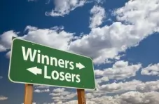 A photo of a green road sign featuring ‘Winners’ and ‘Losers’ in text with white arrows pointing in opposite directions